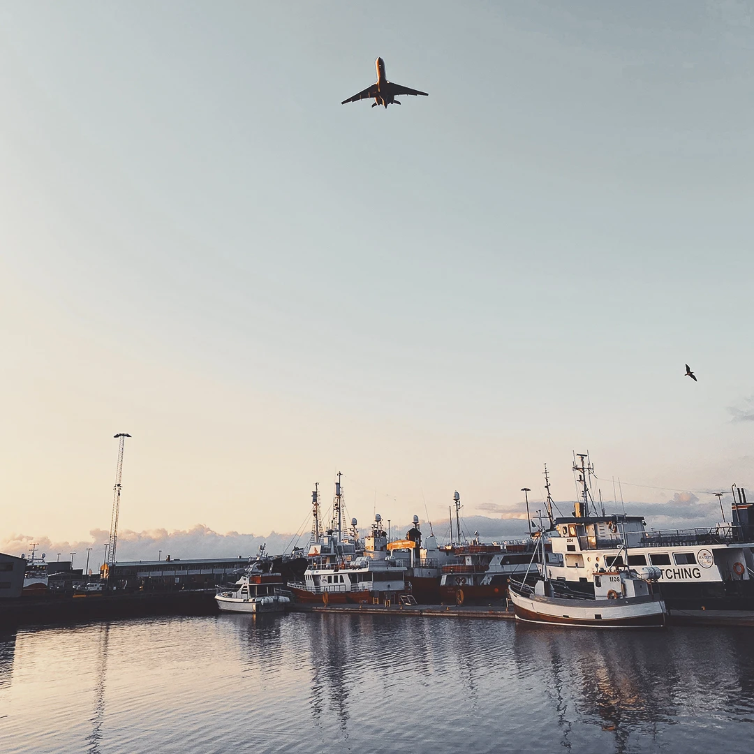 A commercial airplane ascending over a harbour of fishing vessels at golden hour in Reykjavik